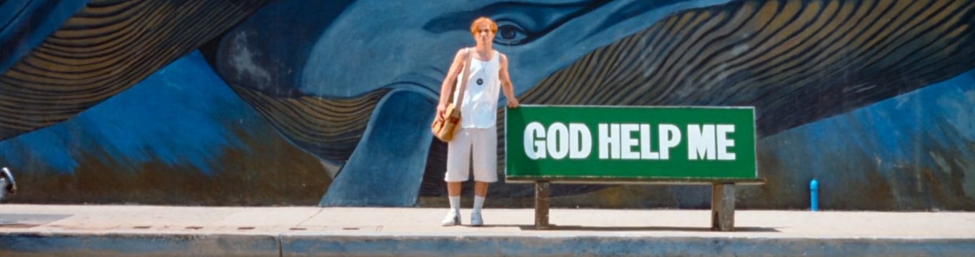 montomgery from nowhere (1997) standing next to a bench that reads 'GOD HELP ME'